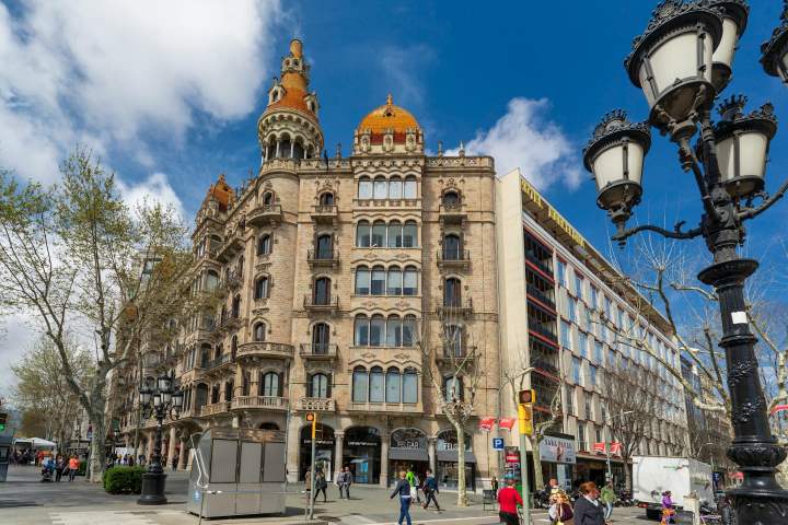 Street view of Barcelona, Spain featuring stunning historic architecture with ornate domes and lively pedestrian streets under a bright blue sky — a must-visit European city in December