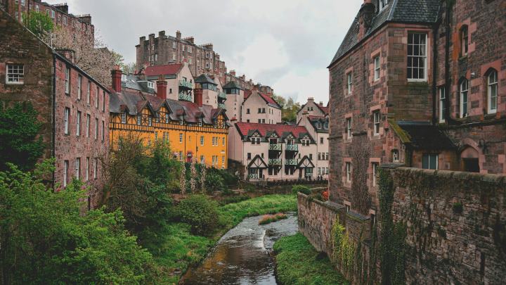 Charming view of Dean Village in Edinburgh, Scotland, featuring colorful historic houses along the Water of Leith surrounded by lush greener