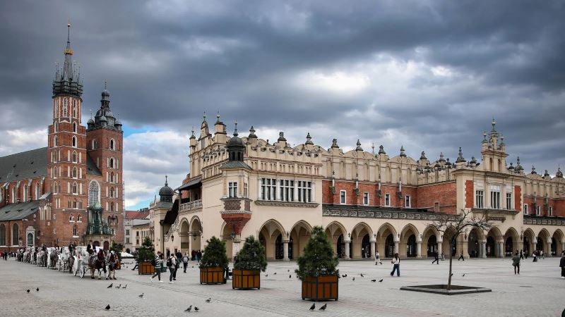 Main Market Square in Krakow, Poland featuring the historic Cloth Hall and St. Mary’s Basilica under a dramatic winter sky
