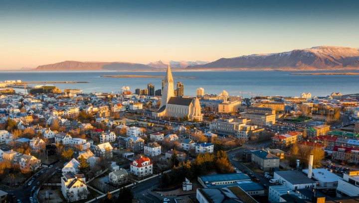 Aerial view of Reykjavik, Iceland in winter, featuring the iconic Hallgrímskirkja Church, colorful houses, and snow-covered mountains by the North Atlantic Ocean