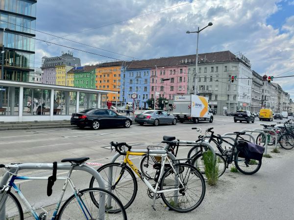 Street view of Vienna, Austria featuring colorful pastel buildings, parked bicycles, and city traffic under a cloudy sky — a vibrant European destination to explore in December with Trekhops