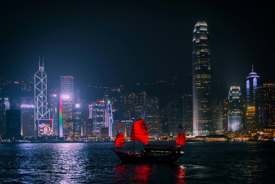A traditional red-sailed junk boat glides across Victoria Harbour against the dazzling night skyline of Hong Kong — one of the top countries to visit visa-free from India.