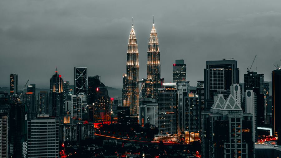 A dramatic cityscape of Kuala Lumpur featuring the illuminated Petronas Twin Towers against a moody evening sky — showcasing Malaysia as one of the top countries to visit visa-free from India.