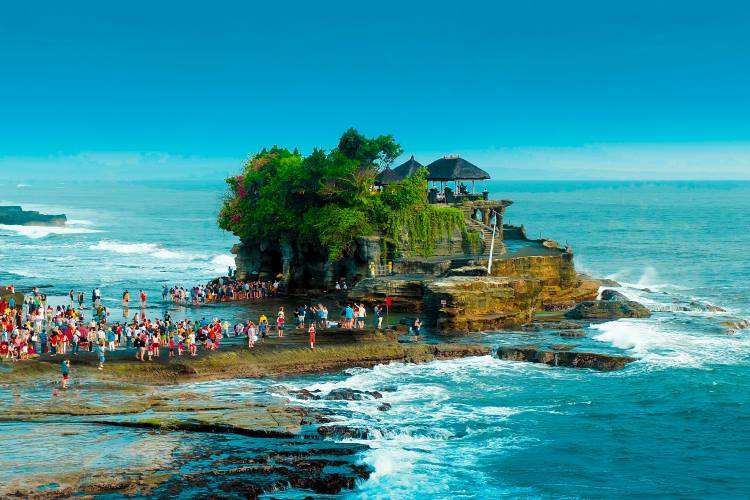 Panoramic view of Pura Tanah Lot, the iconic sea temple in Bali, perched on a rocky outcrop surrounded by crashing waves during the day, a must-visit among temples to visit in Bali.