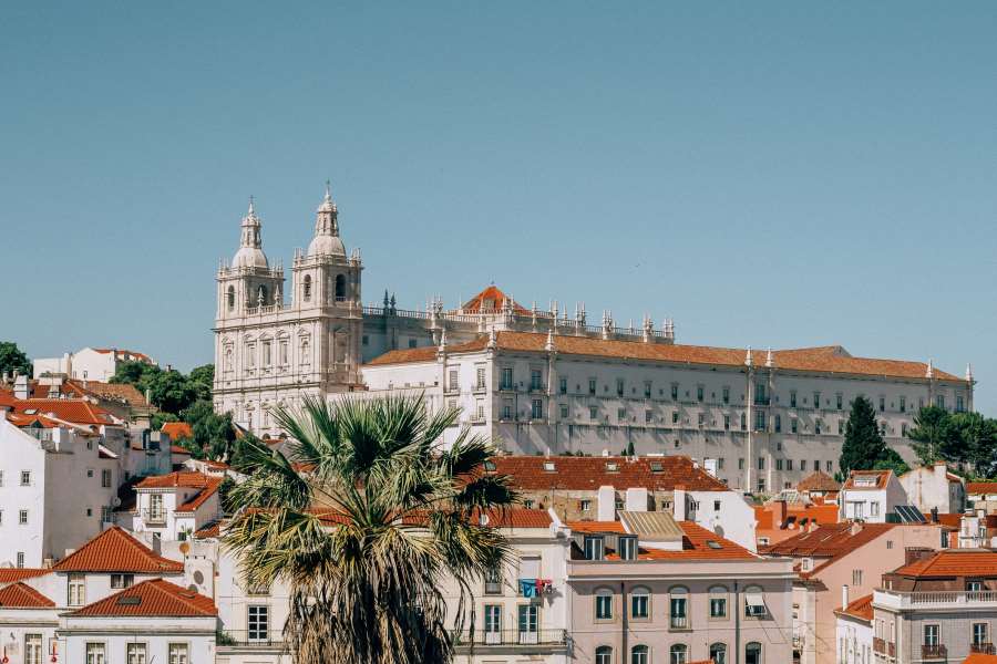 Historic monastery with twin towers overlooking red-roofed buildings in Lisbon, Portugal under a clear blue sky.