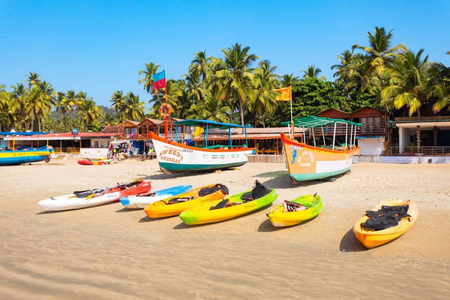 Colorful fishing boats and kayaks on a sandy beach lined with palm trees in Goa, India.