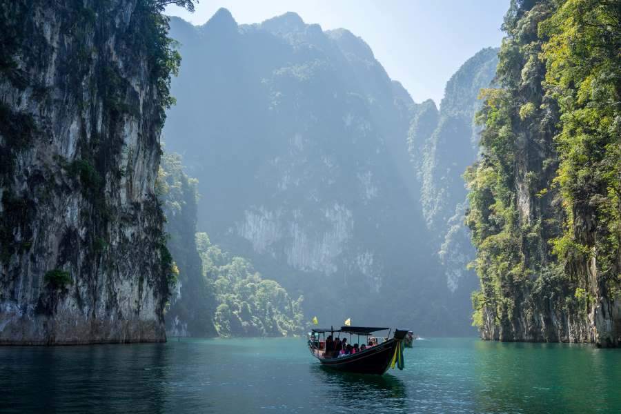 Longtail boat sailing through limestone cliffs on emerald waters at Khao Sok National Park in Thailand.