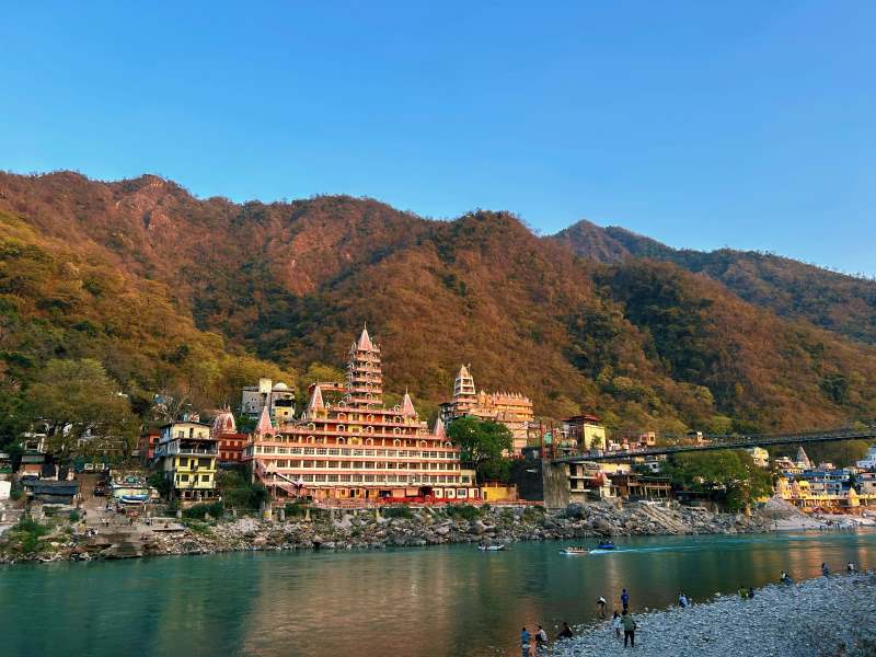 Scenic view of Rishikesh, Uttarakhand with the iconic Trayambakeshwar Temple along the Ganges River and Himalayan mountains in the background.