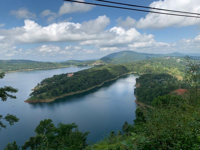 Scenic view of Umiam Lake surrounded by lush green hills and cloudy blue sky in Shillong, Meghalaya, India.