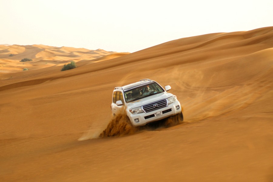 White 4x4 SUV performing high-speed dune bashing on golden desert sand during a Dubai Evening Desert Safari adventure experience.