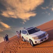 Private desert safari in Dubai with tourists exploring the Lahbab Red Dunes beside a 4x4 Land Cruiser at sunset.