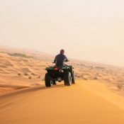 Quad biking in the Dubai desert at sunrise with a rider driving across golden sand dunes, showcasing the thrill of ATV adventure in the Arabian Desert.