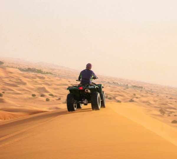 Quad biking in the Dubai desert at sunrise with a rider driving across golden sand dunes, showcasing the thrill of ATV adventure in the Arabian Desert.